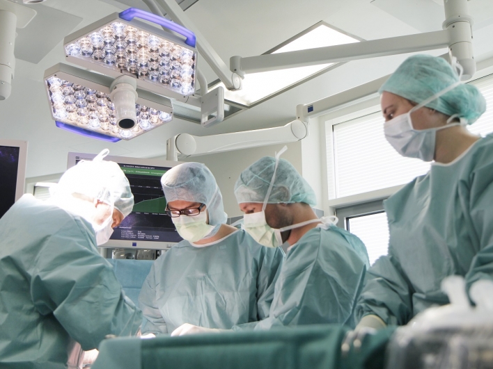 Sechs Ärzte im grünen OP-Kittel und mit Mundschutz stehen am OP-Tisch