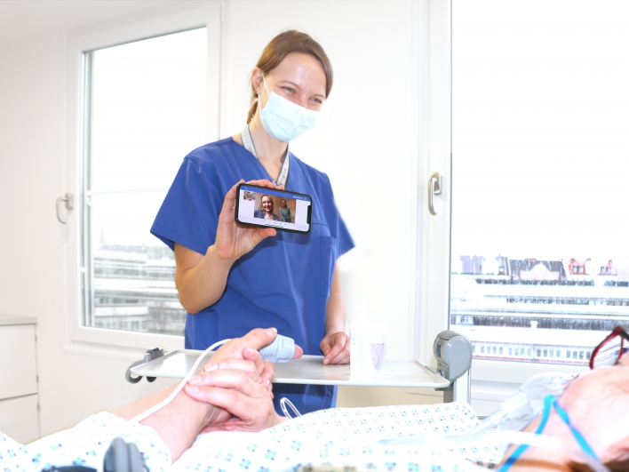 Ein Kommunikationshelfer unterstützt den Patienten bei dem Videoanruf