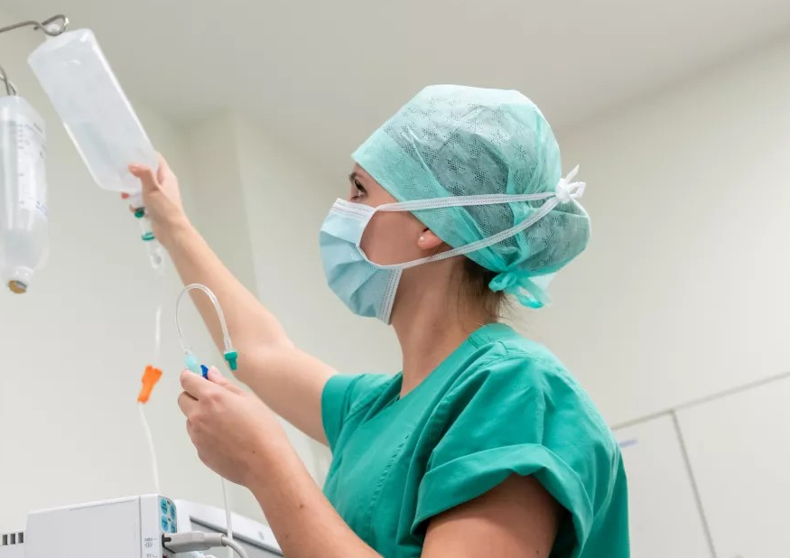 Eine Pflegeauszubildende entfernt eine Infusion vom Infusionsständer