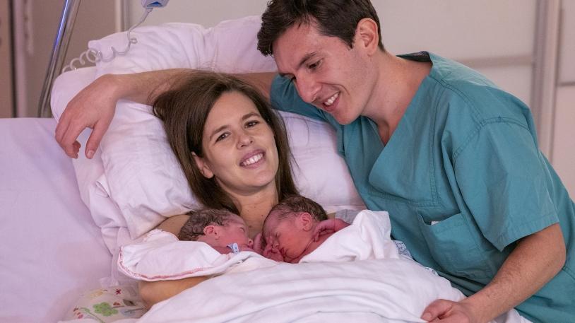 Mutter im Bett liegend mit Zwillingen im Arm, der Vater stehend daneben Mutter im Bett liegend mit Zwillingen im Arm, der Vater stehend daneben