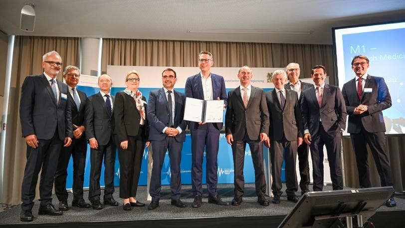 Die Unterzeichnenden des Letter of Intent zur „M1 – Munich Medicine Alliance“, unter ihnen Hubert Aiwanger, Markus Blume und Klaus Holetschek auf einer Bühne stehend. 