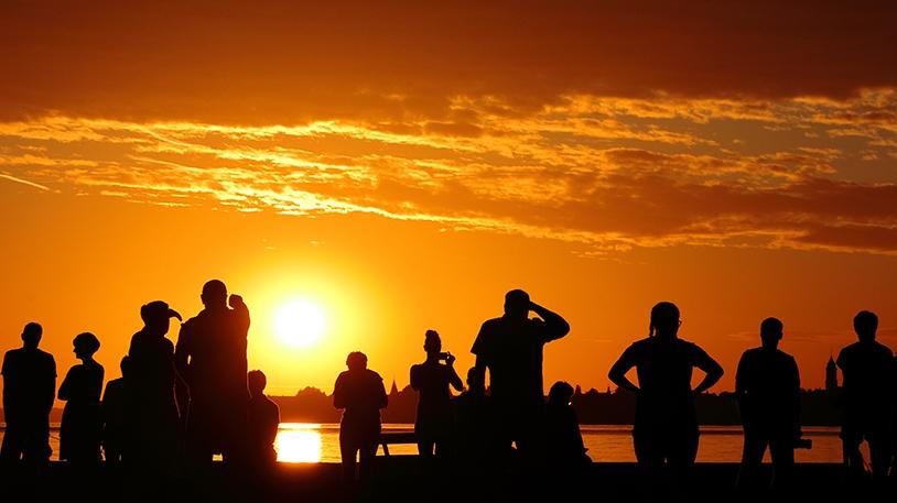 Umrisse von Personen bei Sonnenuntergang an einem See 