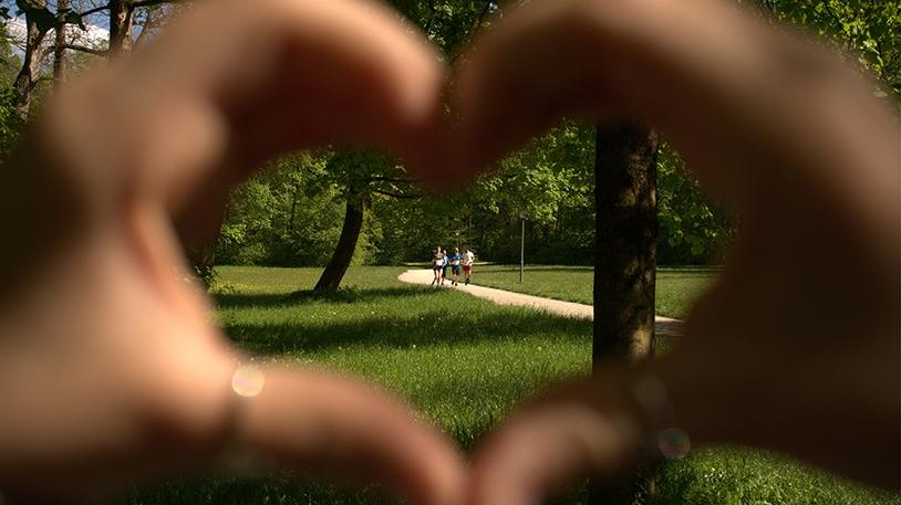 Hände zu Herz geformt mit Joggern in dessen Mitte im Hintergrund 